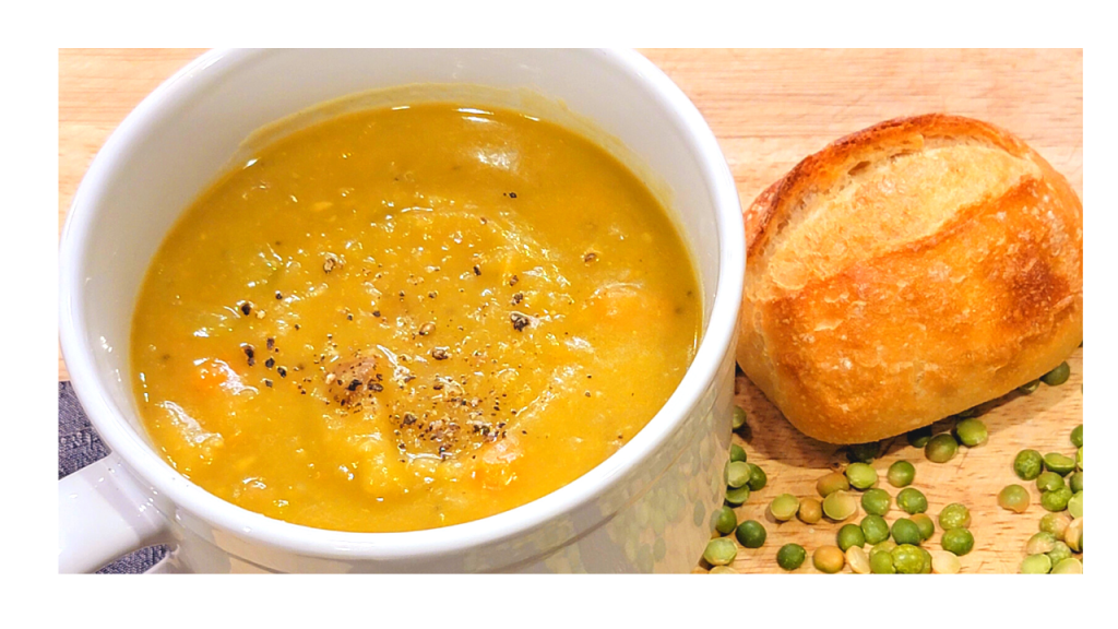 Bowl of split pea soup with a bread roll beside it